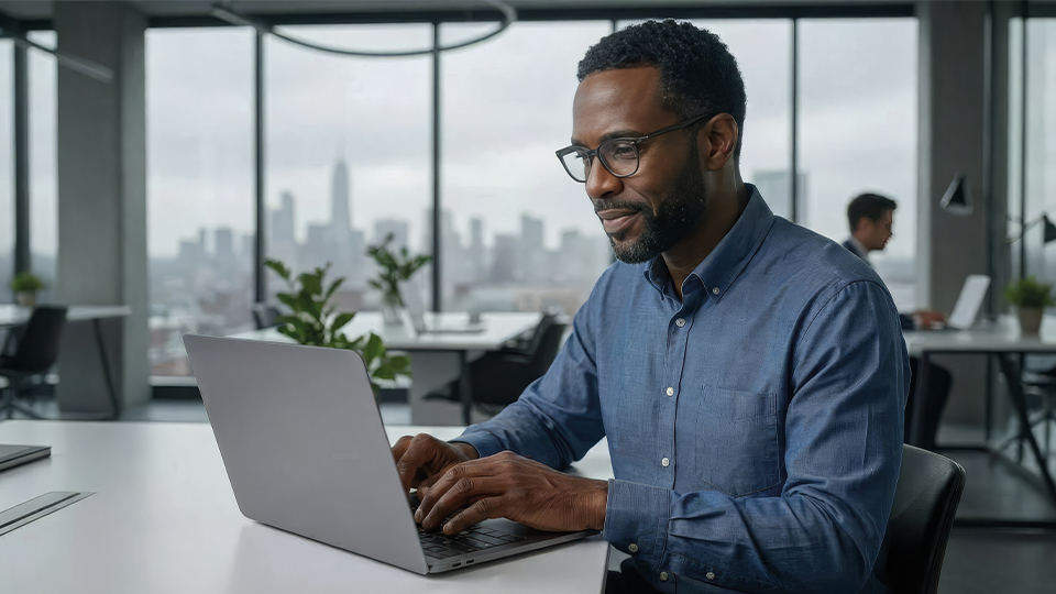A man wearing glasses and seated at a table working seriously at a laptop
