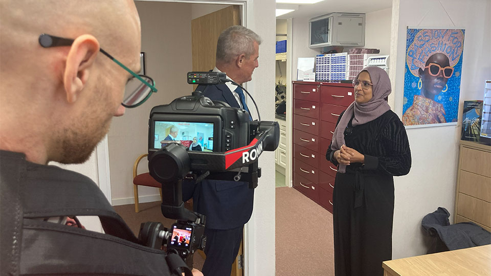 Laurence Derbyshire filming holding a camera with MP Stuart Andrew and optometrist Fatema Soosara in view