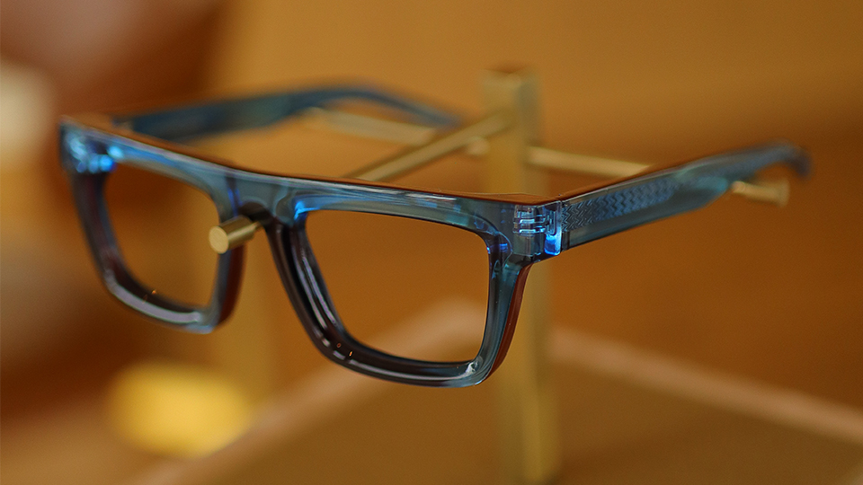 A pair of bold deep blue acetate frames rest on a wooden display