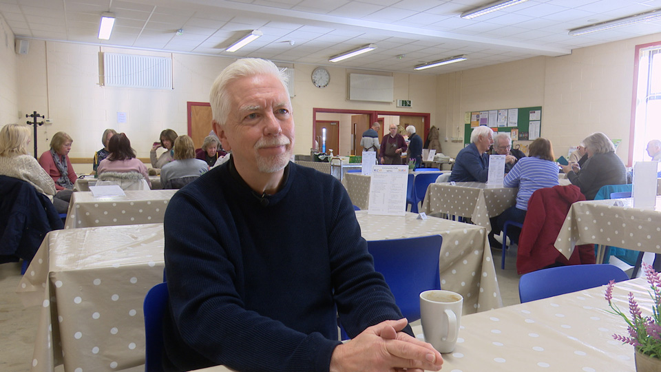 Professor David Thomson is seated at a table in a navy sweater at the Potters Bar community cafe