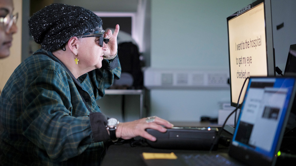 Sheila is photographed over the shoulder as she practices reading using the PRIMA System device