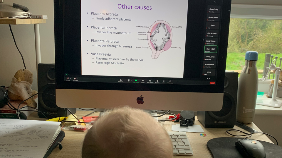A baby is seated on James Brawn’s lap in front of a computer screen