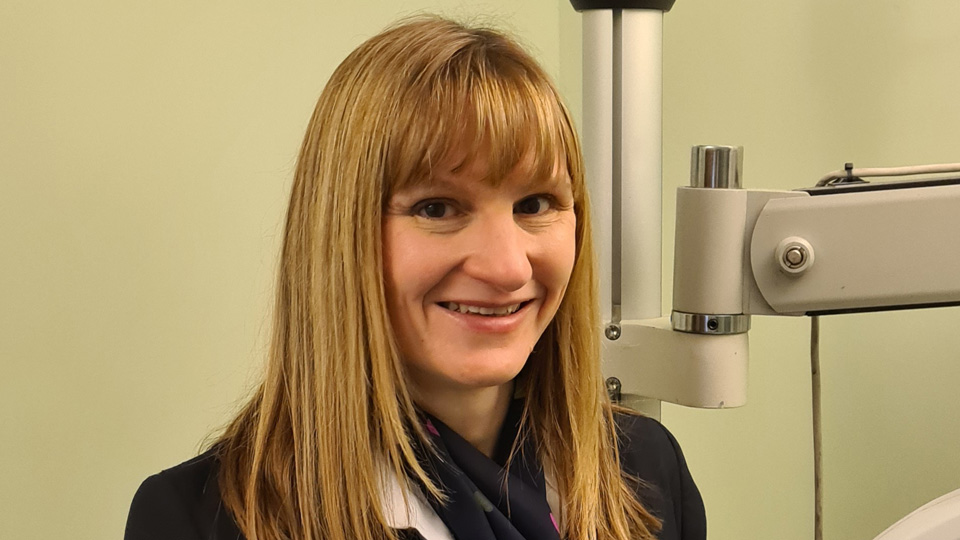 Elaine wears her Specsavers uniform and is smiling in a consulting room, with a device just out of shot behind her