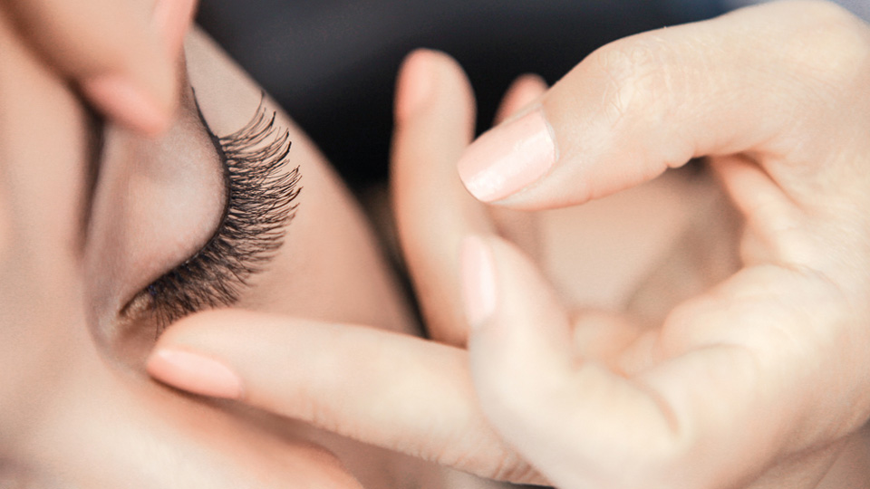 person putting on a fake eye lash onto one eye 