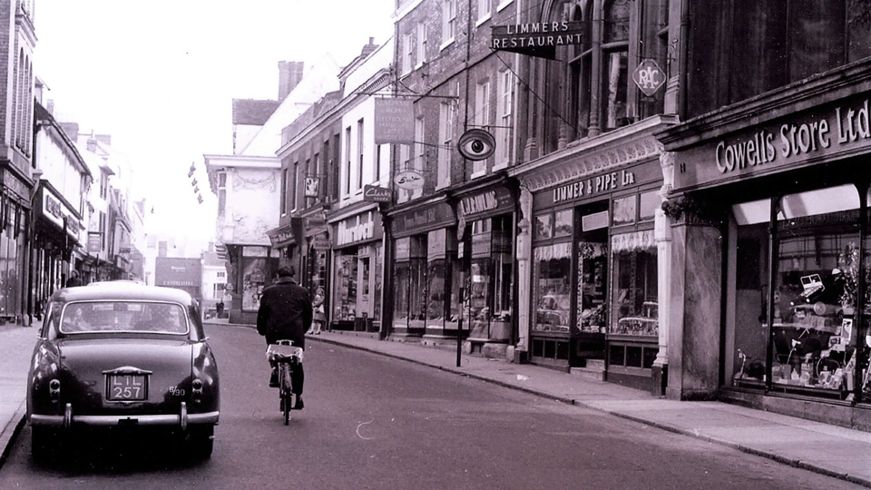 An old black and white photo of A J Rawling Opticians’ original location. A large oval sign hangs above the pavement with a painting of a large eye. 