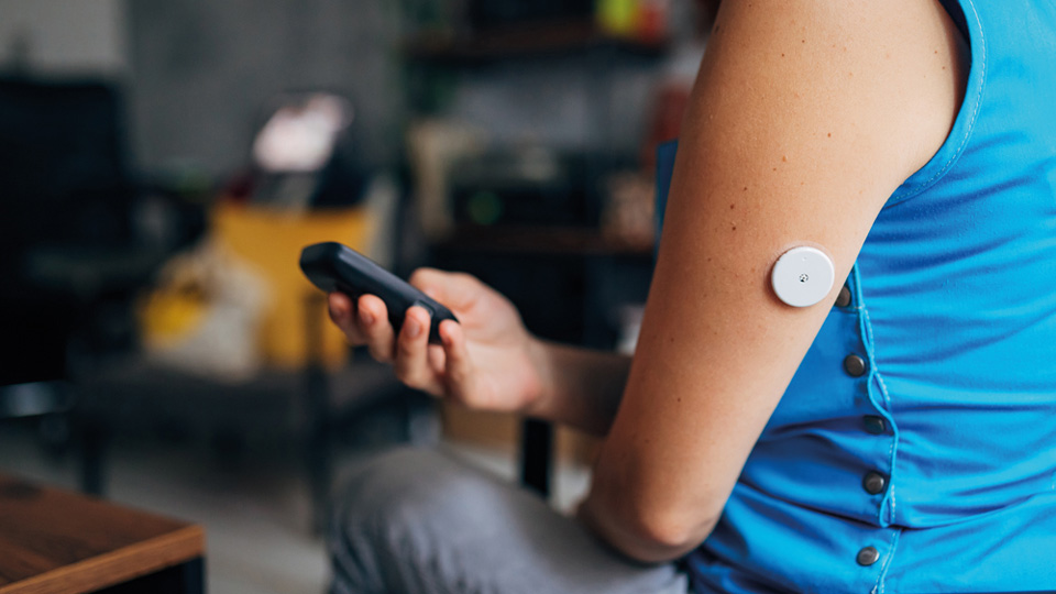 A person with diabetes with a continuous glucoses monitor is checking their results on a device. 