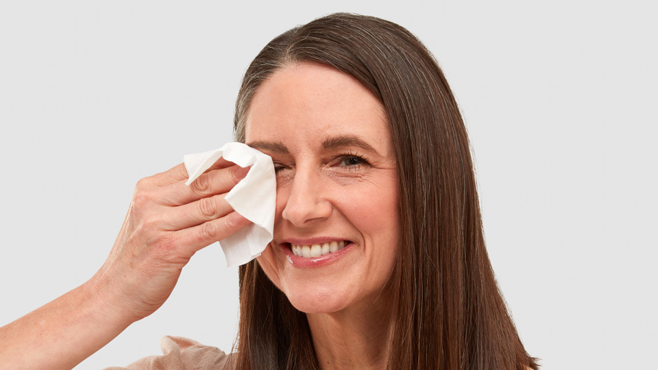 A lady is smiling and holding a wipe up to her eye