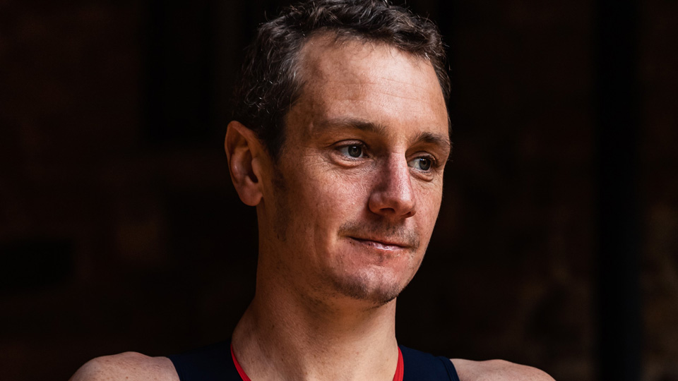 Alistair Brownlee, MBE, is in athletic wear, and looks off to the side against a black background  