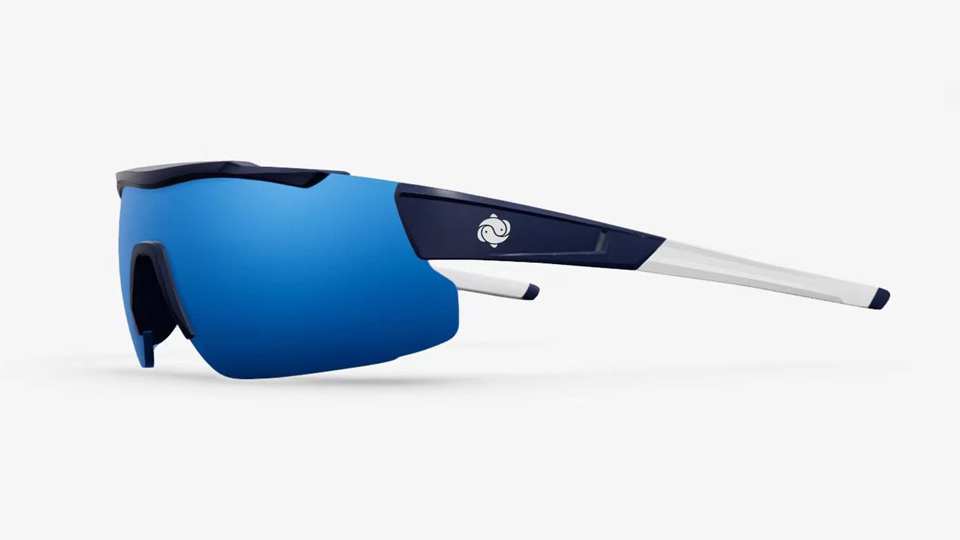 A render of a pair of blue and white wraparound performance frames designed for cyclists. The lenses fade from a light to dark blue. The coral logo stands out in white against navy sides – the logo appears like two simplistic waves or fish shapes curling around each other, reminiscent of a yin and yang symbol