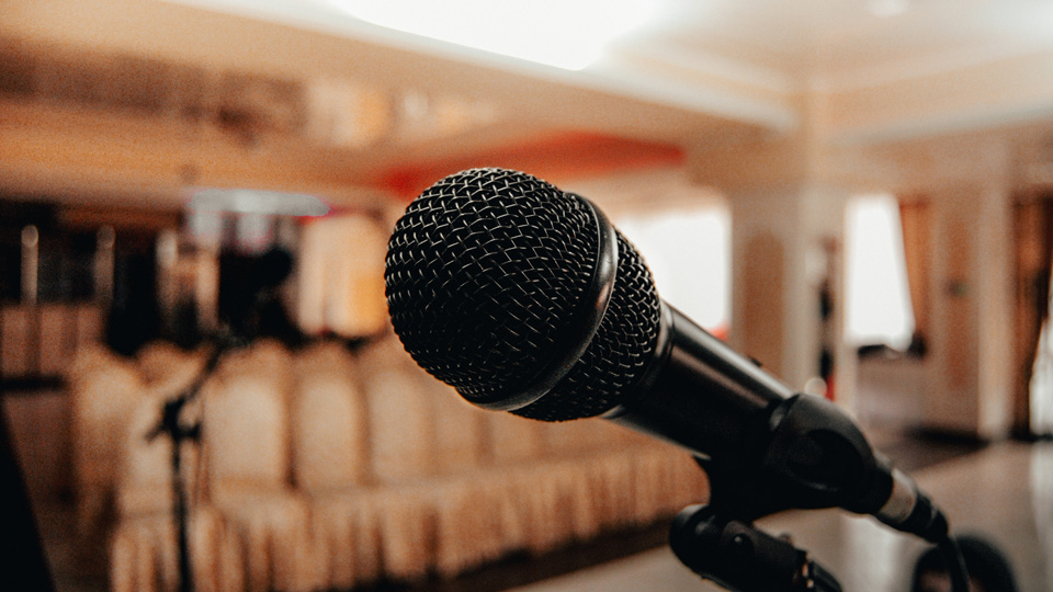 A close-up of a microphone against a background of a venue with several rows of seating