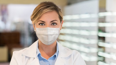 A blonde female optometrist in a face mask looks directly towards the camera