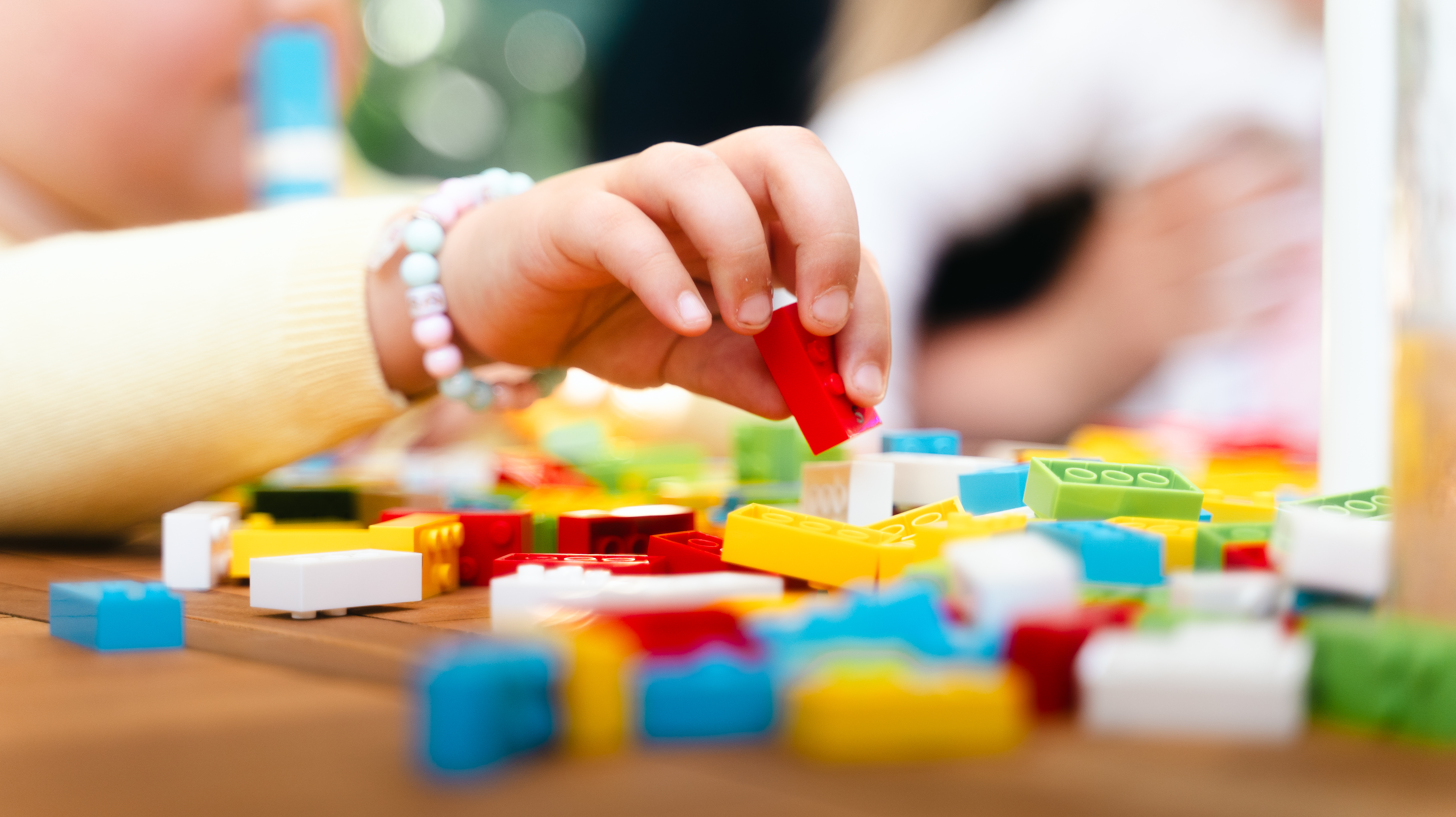 A child’s hand plays with Lego Braille Bricks on a garden table.