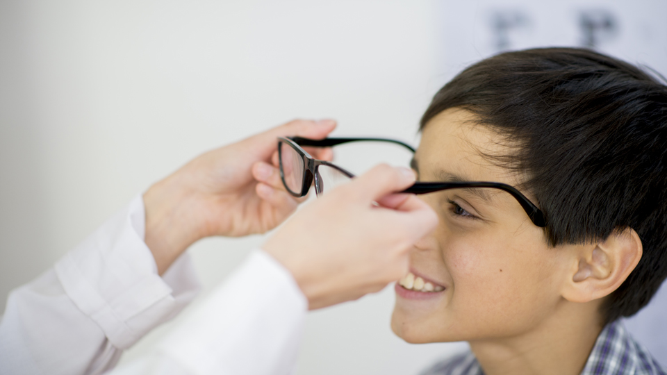 An eye care professional fits a young boy with spectacles 