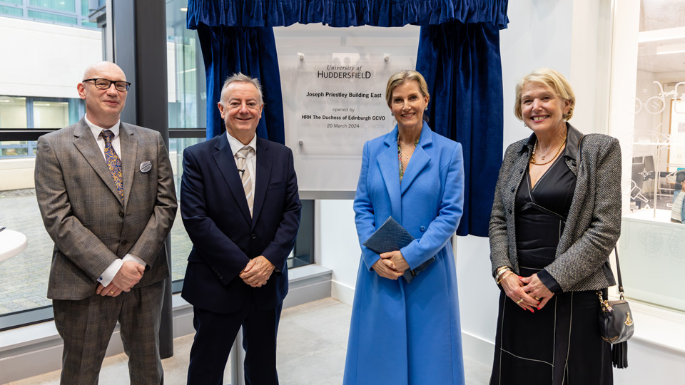Four people standing in front of a plaque at the University of Huddersfield. 