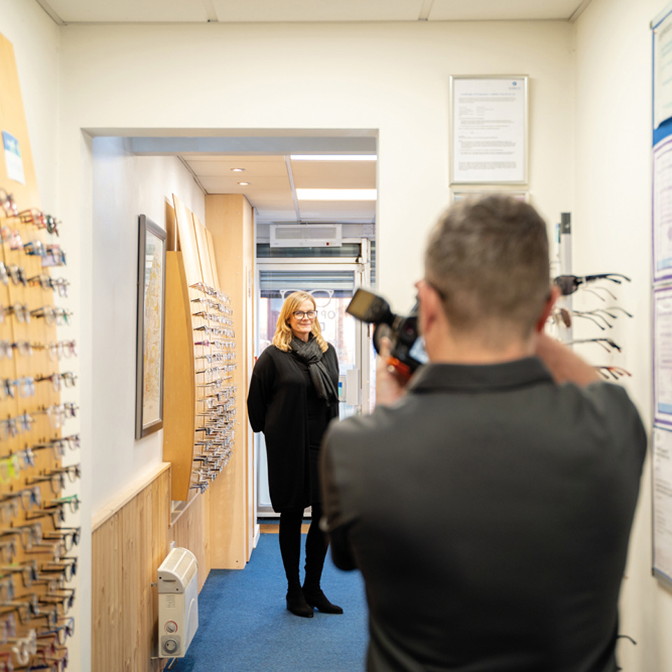Woman standing in an optical practice getting her photograph taken by a professional photographer.  