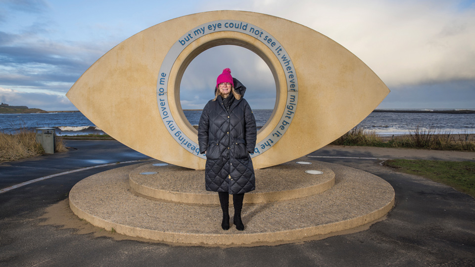 Woman standing in front of the Tyne Eye sculpture at Littlehaven, South Shields. 