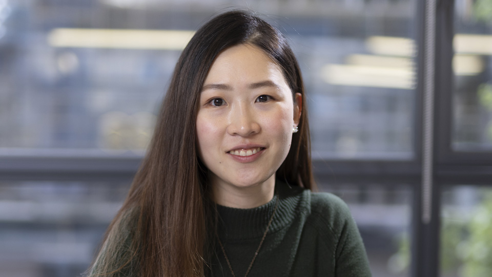 Bonnie Lam, wearing a green jumper, looks thoughtful in front of a large paned window in the AOP offices