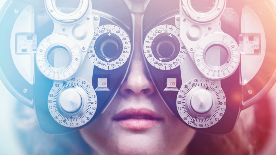 A woman's eyes are tested using a Photopter, determining whether she is due for an update in glasses prescription. Colorful lights add a futuristic feel to the image 