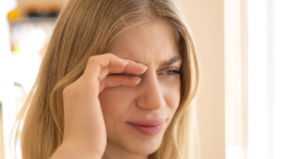 Young blonde woman looks in pain and rubs her right eye