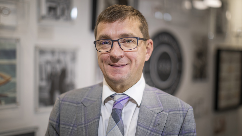  Andrew Bridges is wearing a grey suit and is looking towards the camera in a head and shoulders shot  