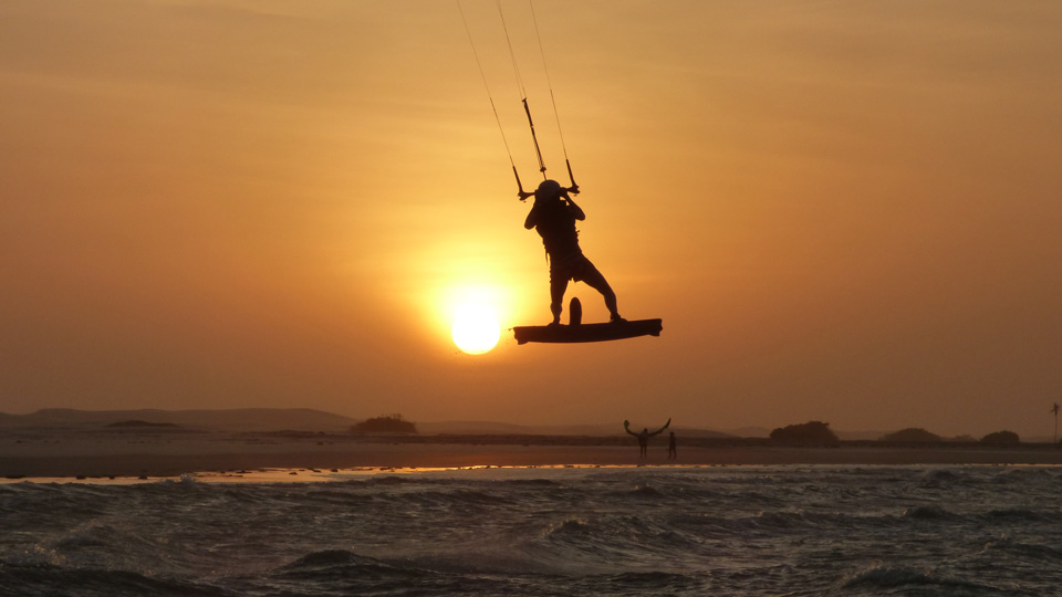 Person kitesurfing, in motion in the air with the sun setting in the background