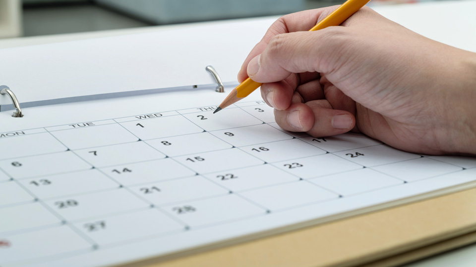 A person writes on a calendar with a pencil 