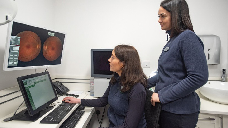Cathy Davis sitting at a desk in practice looking at a scan. Her colleague is standing behind her.
