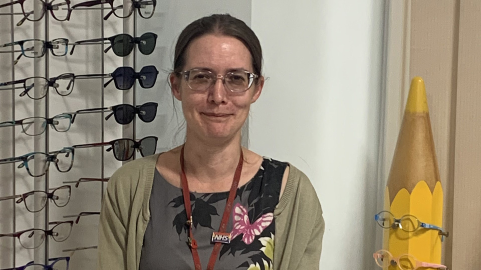 Charlotte Scriven is stood in front of a display of frames and is wearing a green cardigan 