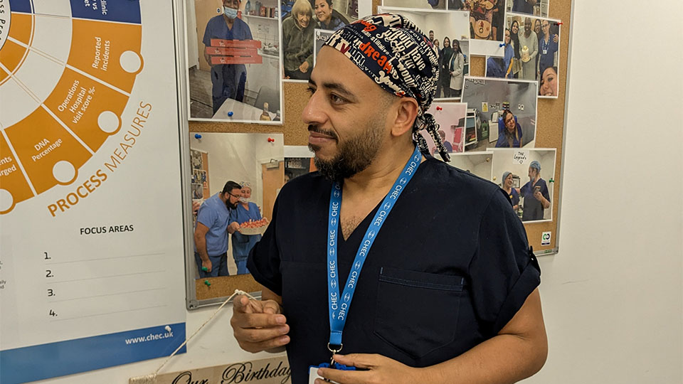Side profile of a male ophthalmologist wearing dark blue scrubs, a light blue lanyard  