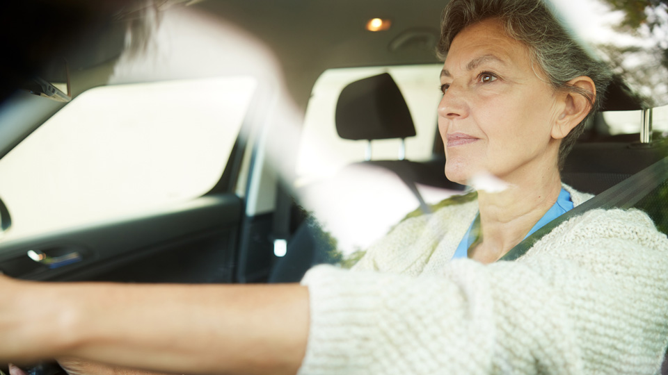 Female seated in a car wearing a blue top and white cardigan 