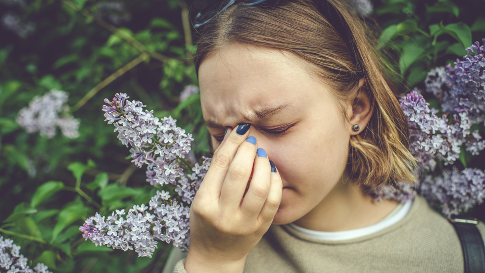 Girl with allergy sneezing and cleaning nose in park near blooming flowers in springtime