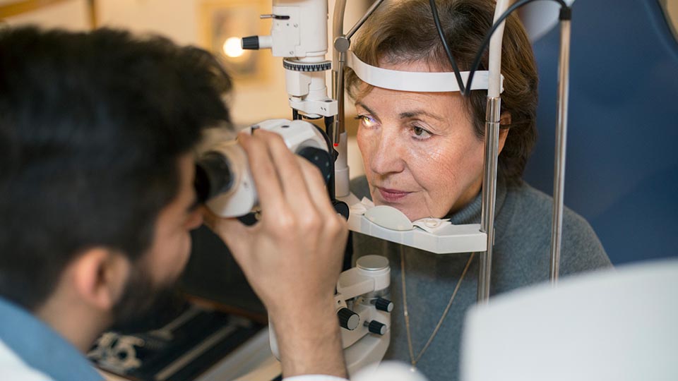 An eye care professional conducts an eye exam on an older woman