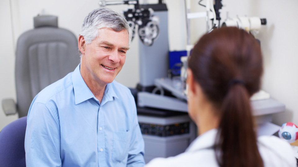 Senior man smiling in an opticians testing room talking to the optometrist 