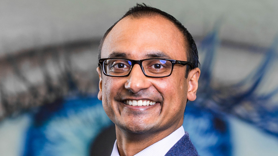 Navneet Gupta is wearing a dark grey suit and smiling widely at the camera  