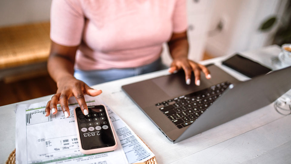 A woman manages her finances, using a calculator and laptop