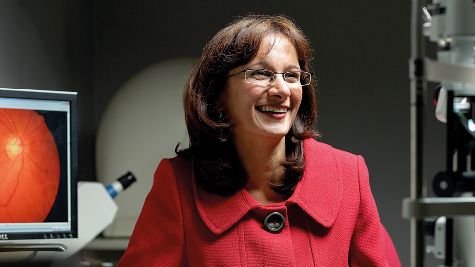 Shahina Pardhan is wearing a red jacket and smiling off camera in a dark room
