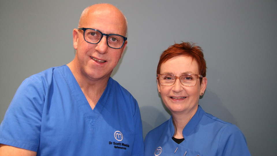 Dr Scott Mackie with his wife, IP optometrist and fellow practice owner Dr Roisin Mackie, both dressed in blue scrubs 