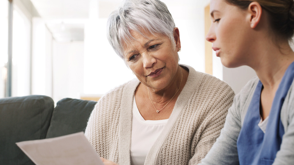 Two people sitting down. One is a medical professional who is holding a piece of paper