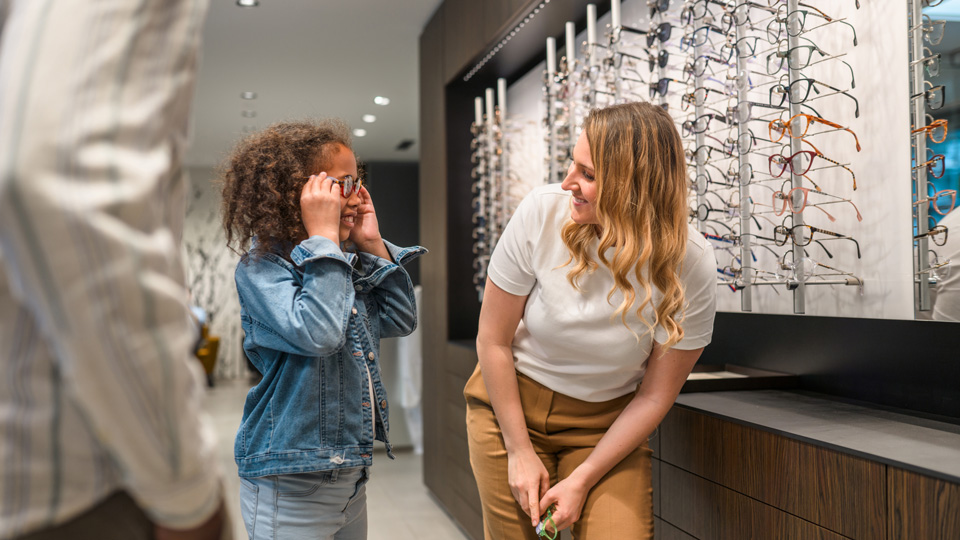 A female optometrist helps a young girl try on glasses