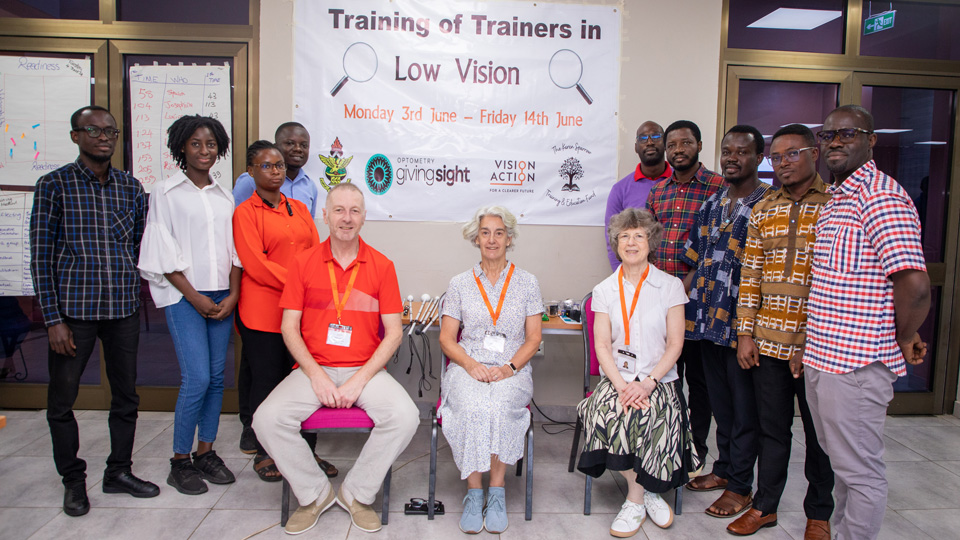 A group photo of Vision Action volunteers and course attendees stand around a sign for Training of Trainers in Low Vision