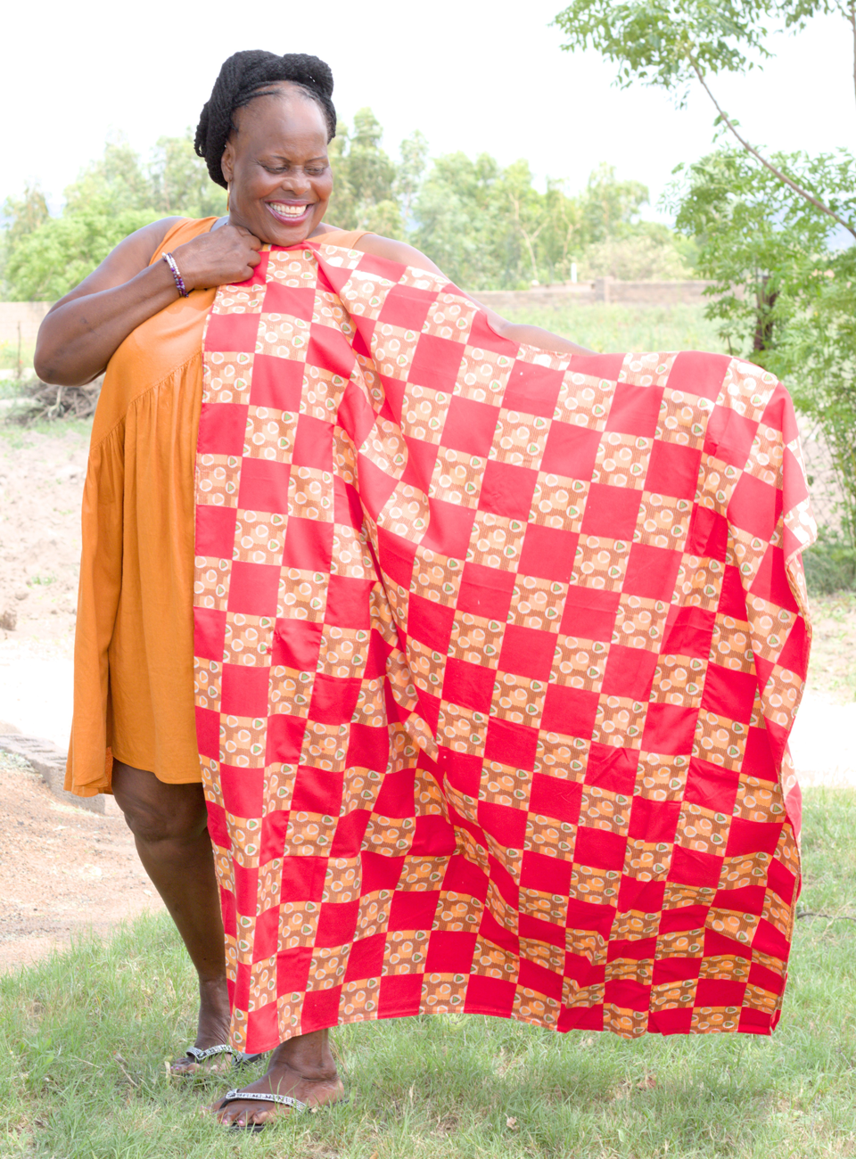 A female dressmaker, Aquila, holds out a red and orange cloth she designed and created on returning to work after her cataract surgery 