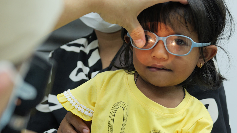 A toddler, sitting in her parent’s lap, has her vision tested by an eye care professional