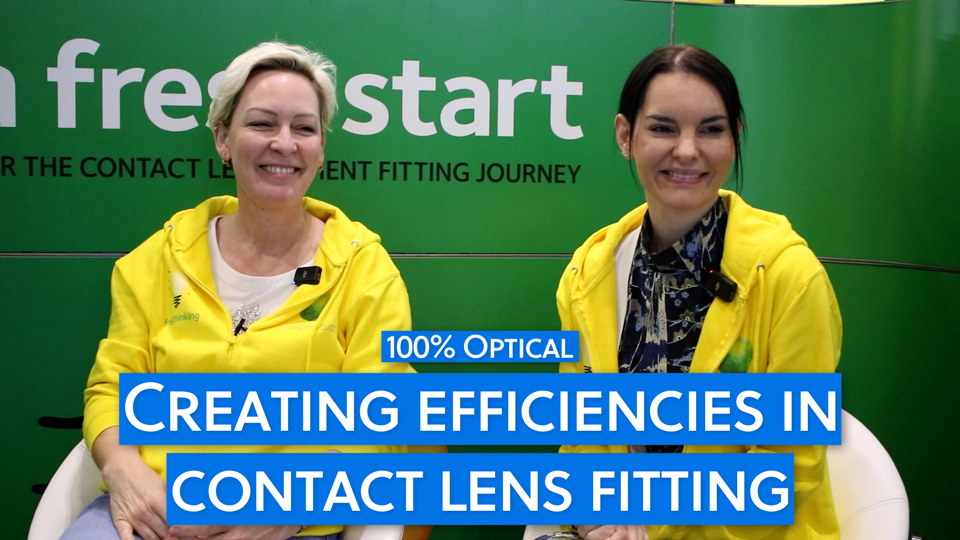 Sarah Weston and Christina Olner sit together on the green CooperVision stand, both wearing bright yellow hoodies with the Fresh Thinking campaign logo