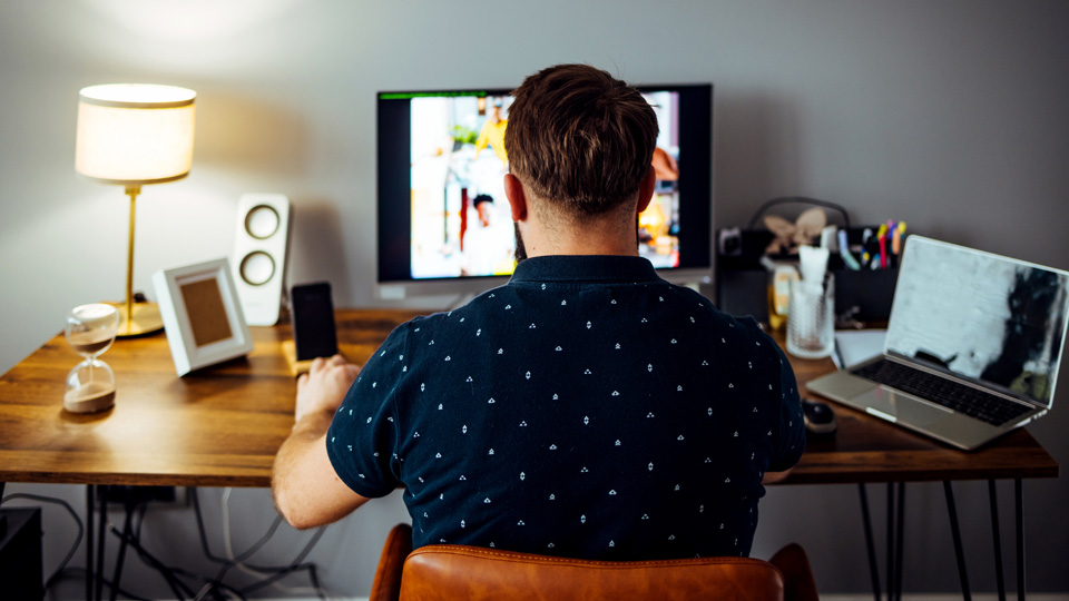 Businessman in a blue shirt with back to camera on a video conference at home