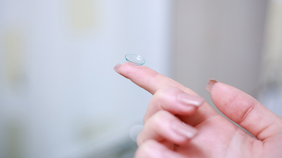 A contact lens rests on a woman’s forefinger.