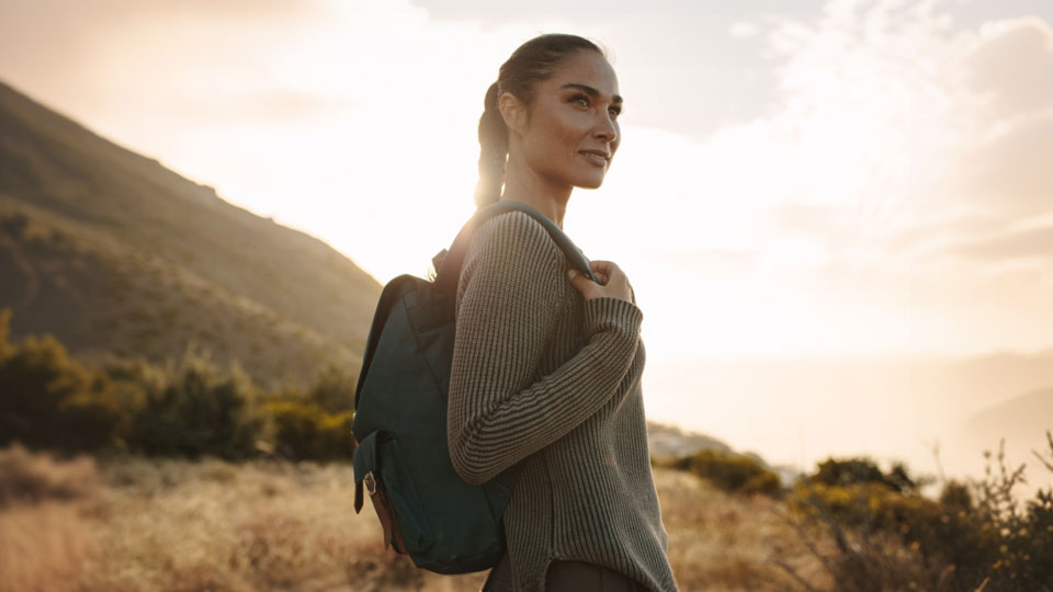 Woman walks in a natural landscape and is half-turned towards the camera, posing in the setting sun