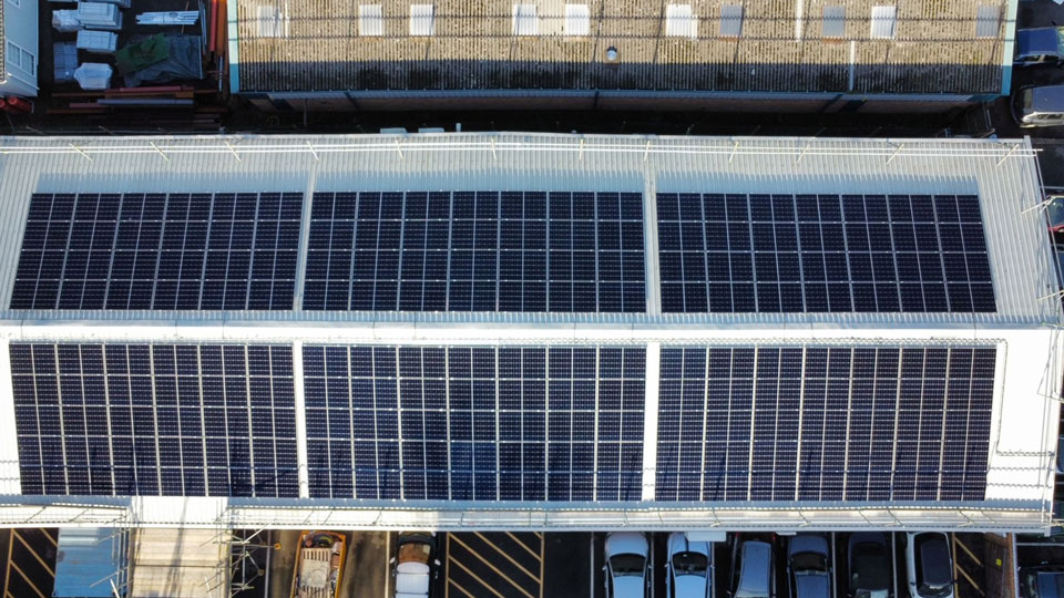 A photo taken from above of the roof of a warehouse building, lined with rows of solar panels