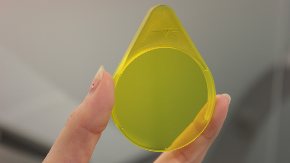 A close up of a fluorescein filter held between the thumb and forefinger