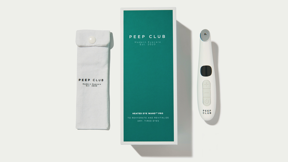 A flatlay of the teal green box with the Peep Club logo in the centre, to the right is the Heated Eye Wand Pro, and on the left is a case