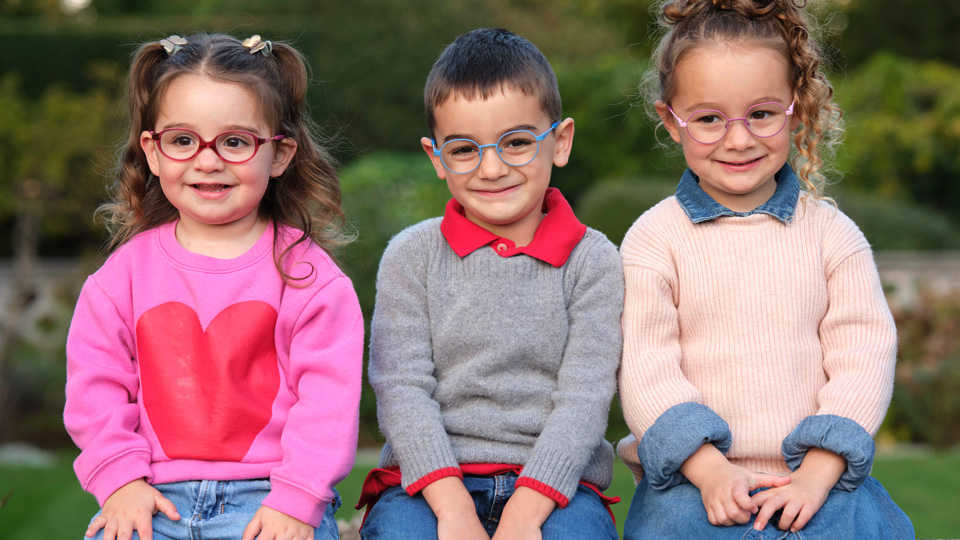 Three children sit in a row, all in colourful eyewear 